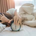 Une femme tient son réveil dans son lit