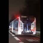 Deux jeunes hommes accrochés à l'arrière d'un bus en marche