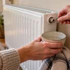 Une main ouvre la vis de purge d'un radiateur à eau chaude avec une clé, un petit récipient posé dessous