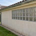 Mur latéral d'un garage en limite de propriété, percé de pavés de verre, vu depuis le jardin voisin