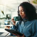 Jeune employée buvant son café devant son ordinateur et sa tablette
