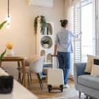 Jeune femme avec sa valise ouvrant les fenêtres dans un appartement