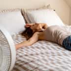 Jeune femme ayant chaud allong&eacute;e sur lit avec un ventilateur