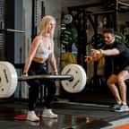 une femme soulevant une barre avec des poids accompagnée d'un coach de sport