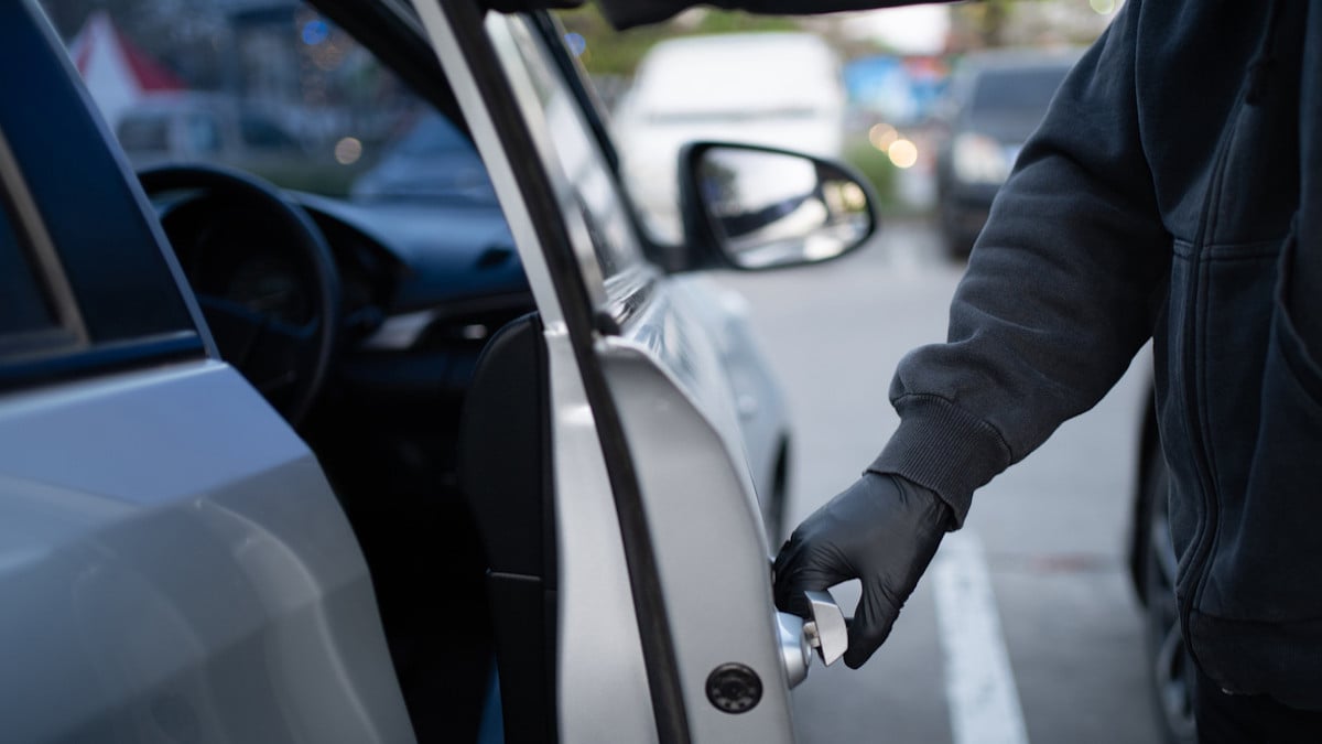 Un voleur en train d'ouvrir la portière d'une voiture 