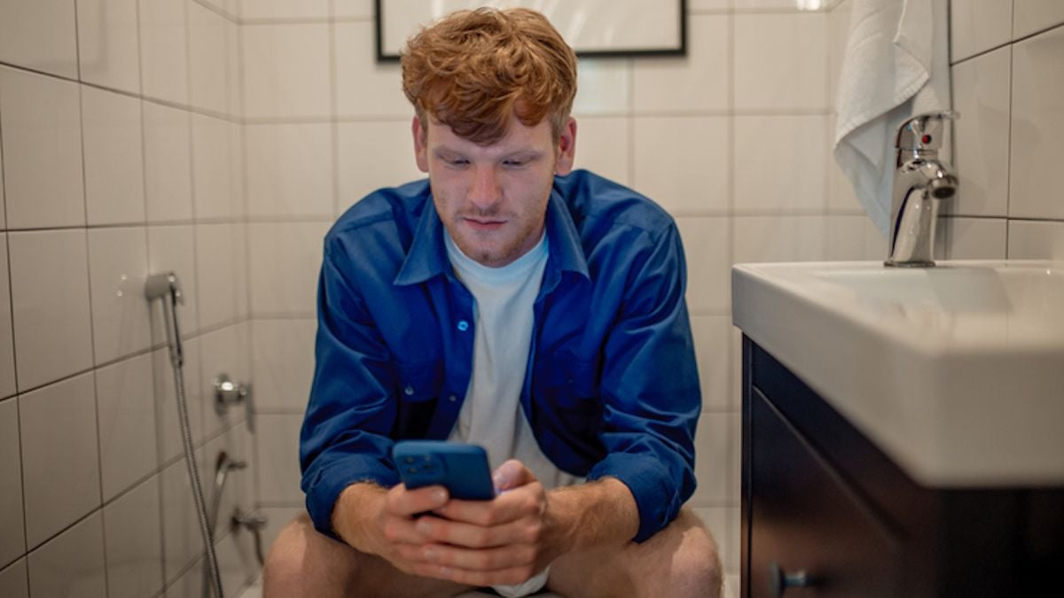 Un homme assis aux toilettes avec son téléphone