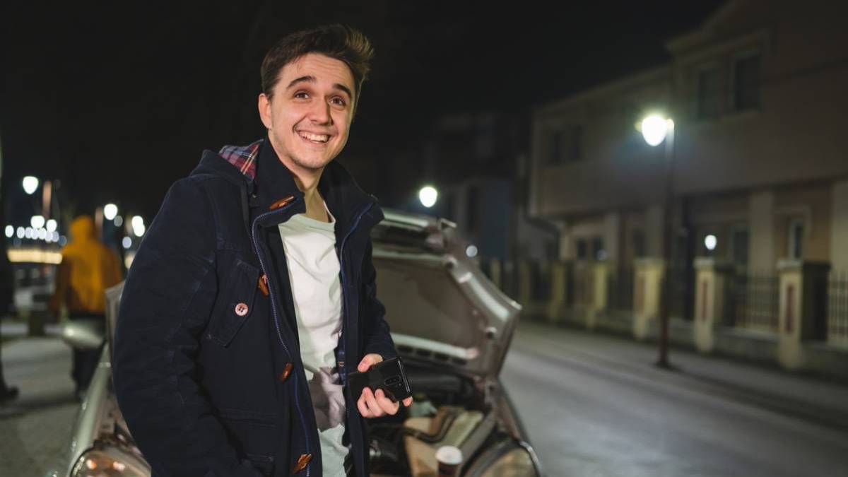 Jeune conducteur debout près de sa voiture capot ouvert