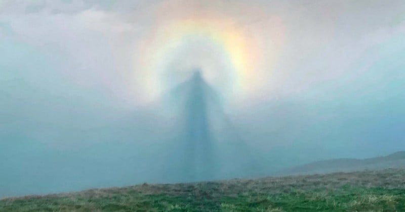 Un randonneur photographie une silhouette angélique dans le ciel entouré d'une auréole arc-en-ciel