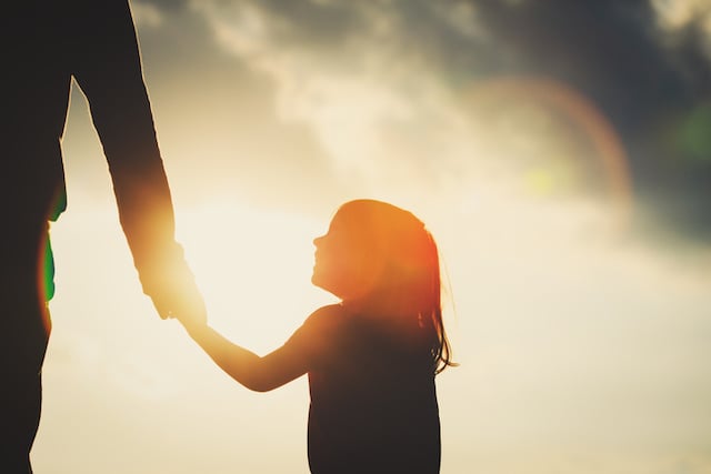 Silhouette d'une petite fille tenant la main de la mère au coucher du soleil 