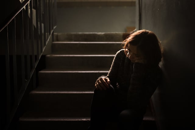 Une jeune fille triste assise sur des marches d'escaliers dans le noir