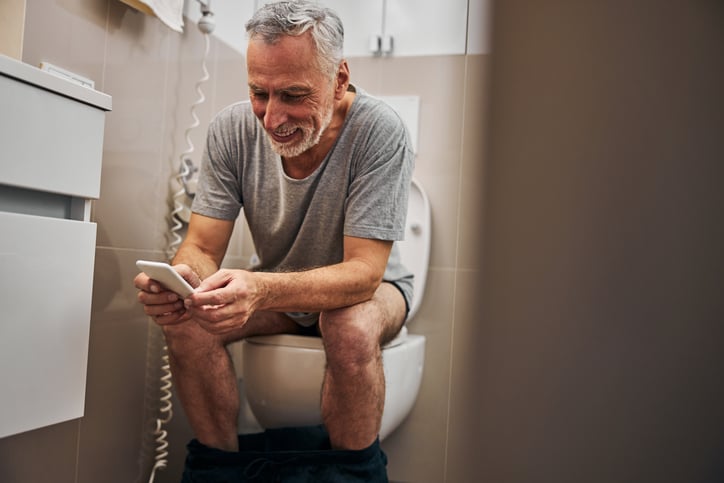 Un homme assis aux toilettes avec son téléphone