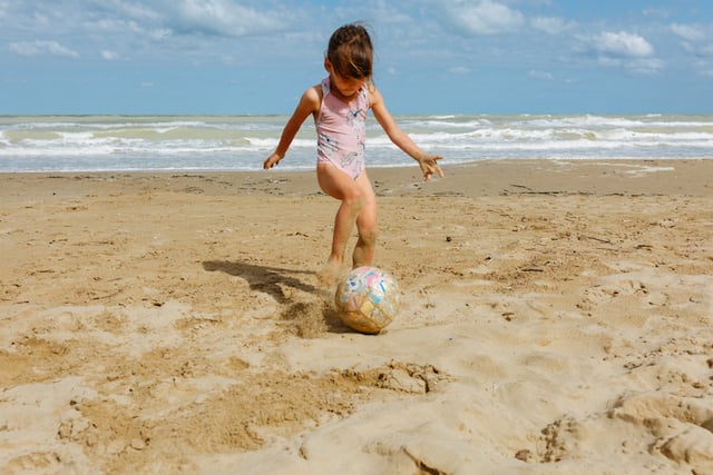 Une petite fille en train de jouer au ballon sur une plage 