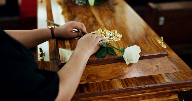 Une femme dépose sur une rose blanche sur un cercueil 