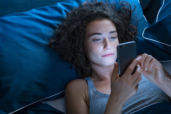 Une femme scrolle son téléphone la nuit