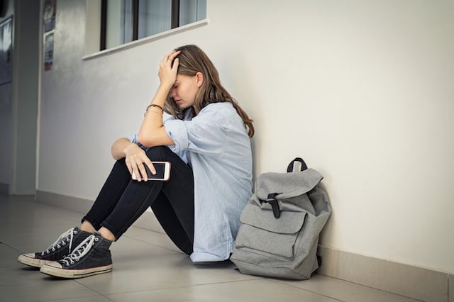 Une élève triste adossée contre le mur de sa salle de classe
