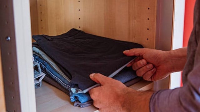 Un homme en train de ranger ses pantalons dans une armoire 