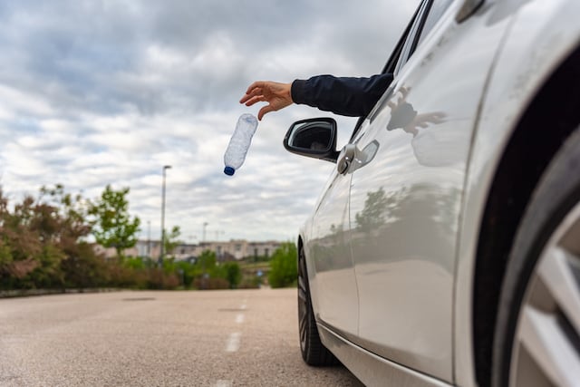 Main d&rsquo;un homme jetant une bouteille d&rsquo;eau usag&eacute;e par la fen&ecirc;tre de sa voiture sur la route