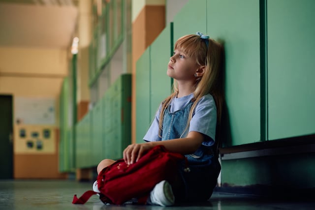 Une petite fille pensive assise seule dans le couloir de l&rsquo;&eacute;cole