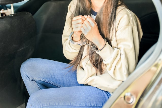 Une femme menott&eacute;e assise dans une voiture de police