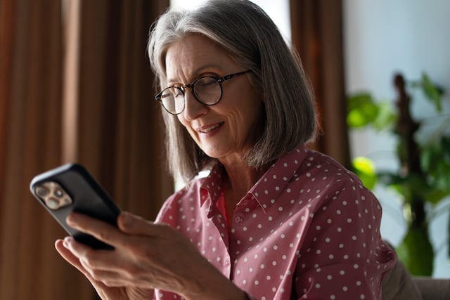 Une femme âgée heureuse en train de lire un message sur son téléphone protable