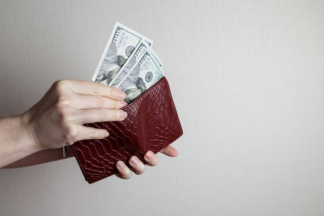 Une main de femme qui sort trois billets de son porte-monnaie