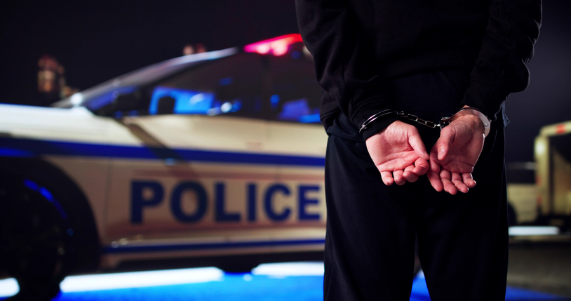 Un homme menott&eacute; devant une voiture de police