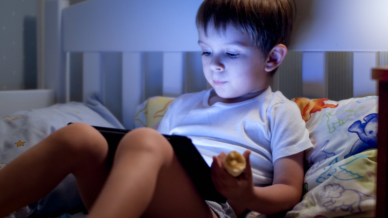 Un enfant utilise une tablette dans son lit