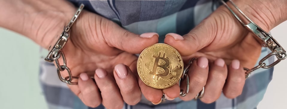 Personne menott&eacute;e, tenant un jeton qui illustre un bitcoin