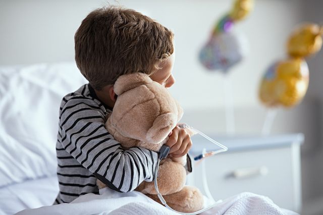 Un enfant enla&ccedil;ant un ours en peluche depuis son lit d'h&ocirc;pital