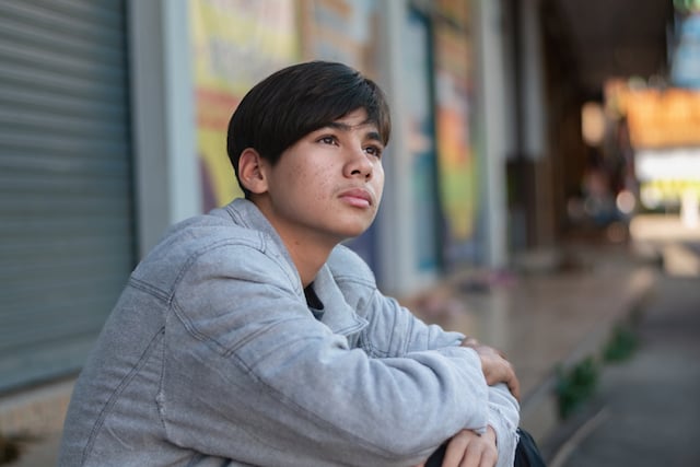 Un adolescent assis sur un trottoir 