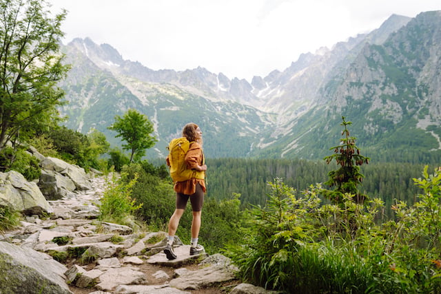 Femme heureuse avec un sac &agrave; dos de randonn&eacute;e jaune profitant du paysage de montagne
