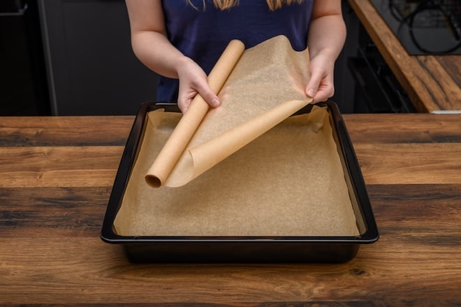 une femme d&eacute;roulant du papier cuisson sur une plaque