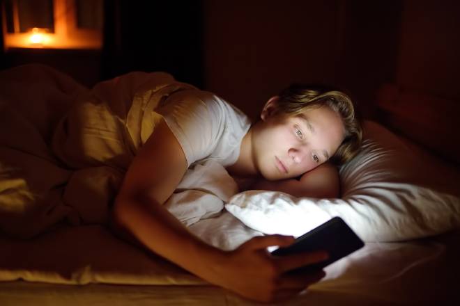 Adolescent sur son t&eacute;l&eacute;phone portable dans son lit