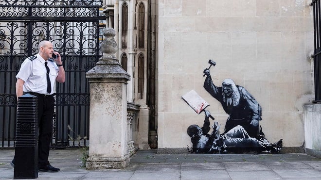 Oeuvre de Banksy sur le mur d'un tribunal londonien protégée par un agent de sécurité