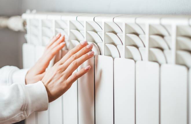 Une femme se r&eacute;chauffe les mains devant un radiateur