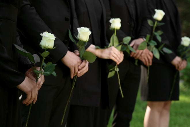 Famille habillée de noir et tenant une rose blanche lors d'une enterrement