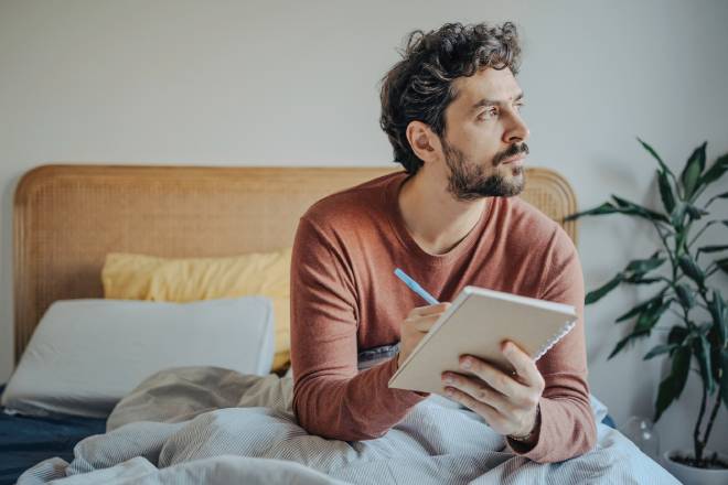 Homme &eacute;crivant dans son journal sur son lit