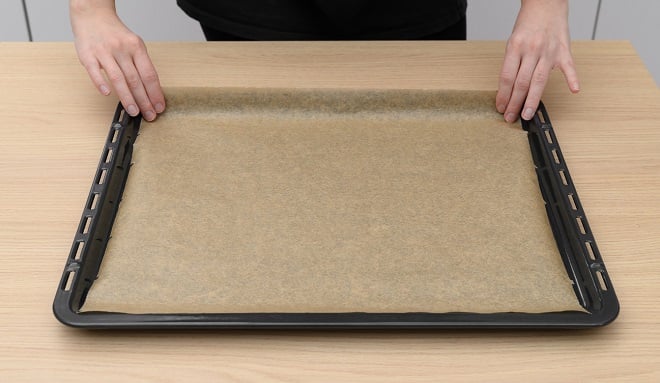 Personne mettant du papier sulfurisé sur une plaque de cuisson