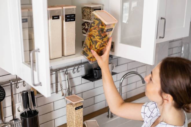 Jeune femme rangeant des p&acirc;tes dans un placard &agrave; cuisine