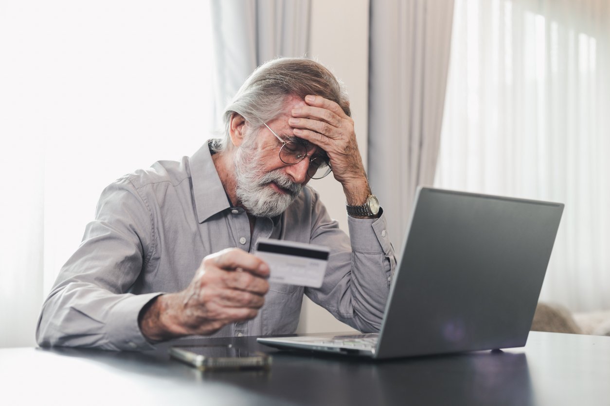 Retraité inquiet tenant sa carte de crédit devant un ordinateur portable